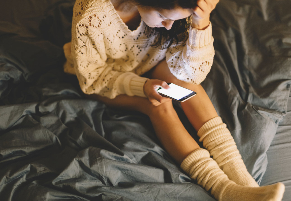 Girl in bed texting on smartphone. iStock image.